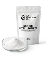 A white stand-up pouch labeled 'JNA INGREDIENT CO. SODIUM HYALURONATE' stands behind a small clear glass dish filled with white powder on a clean white background.
